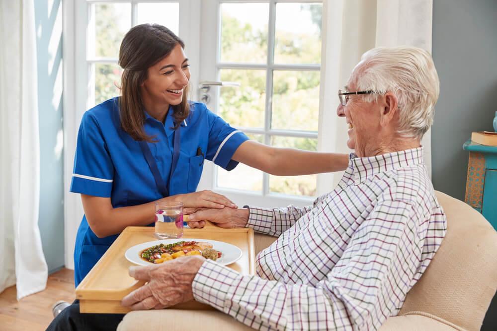 A nurse assists a man with a meal on a tray while in assisted living near Lewiston, MN.